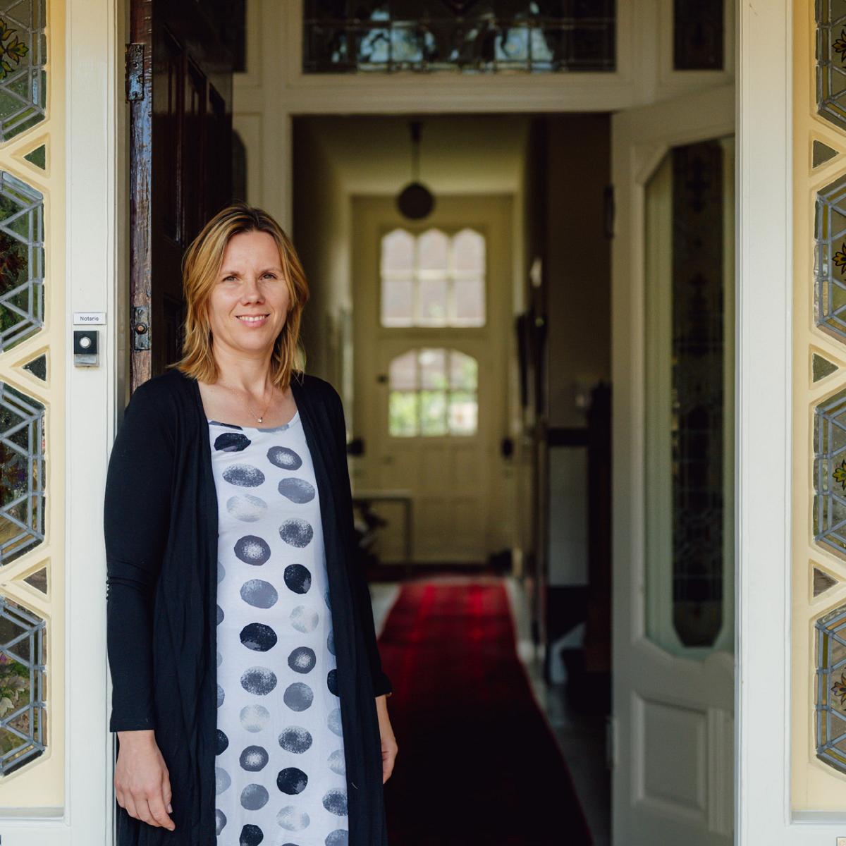 Twee notarismedewerkers in gesprek aan vergadertafel op notariskantoor, met laptop en dossiers in een lichte kantoorruimte