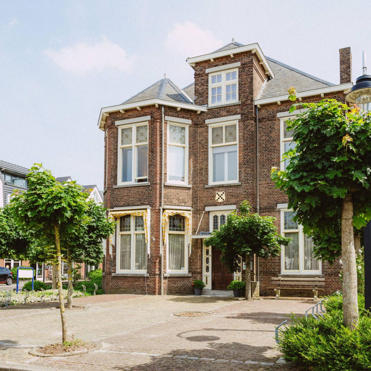 Vooraanzicht van het bedrijfspand van Notariskantoor Voorhout met op de voorgrond bomen. 