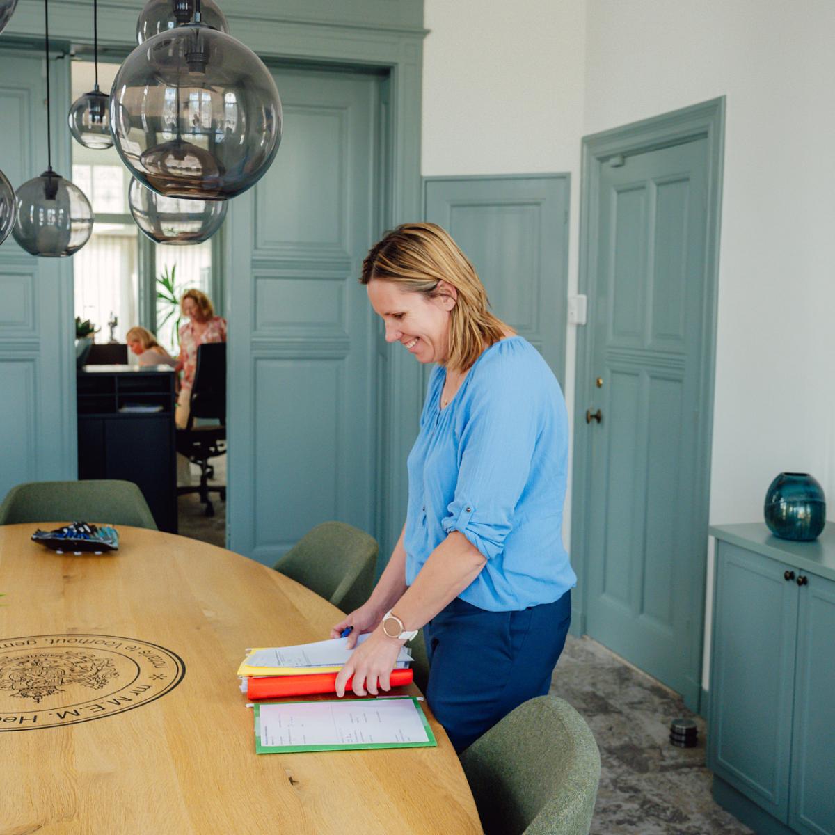 Medewerker van Notariskantoor Voorhout legt dossiers klaar op de vergadertafel in een stijlvolle spreekkamer van het notariskantoor.